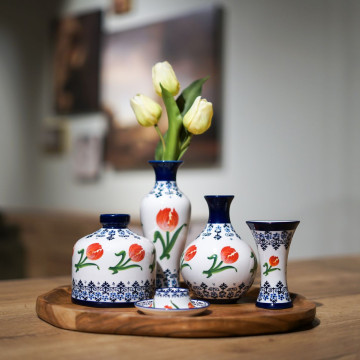 Vier verschillende vaasjes. Een witte achtergrond met onderaan en bovenaan Delfts blauw versiering. In het midden van de vaas rondom oranje tulpen. Een kelkvaasje, buikvaasje, rond vaasje en een slank vaasje.