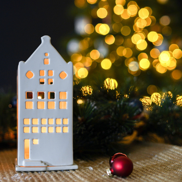 Wit waxinelichthouder huisje op een tafel met kerstdecoraties