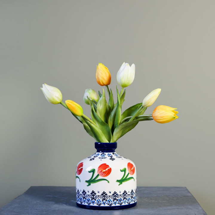 Een ronde vaas met een witte achtergrond met onderaan en bovenaan Delfts blauw versiering. In het midden van de vaas rondom oranje tulpen.