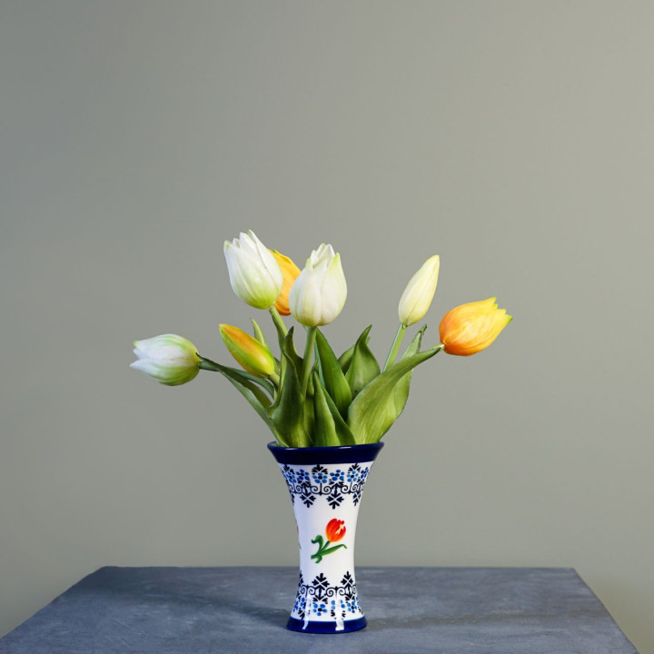 Kelkvaasje met een witte achtergrond met onderaan en bovenaan Delfts blauw versiering. In het midden van de vaas rondom oranje tulpen.